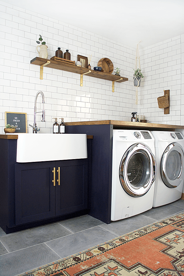 small farmhouse laundry room with navy blue shaker cabinets, large white farmhouse sink, subway tile, wood accents and tile floors