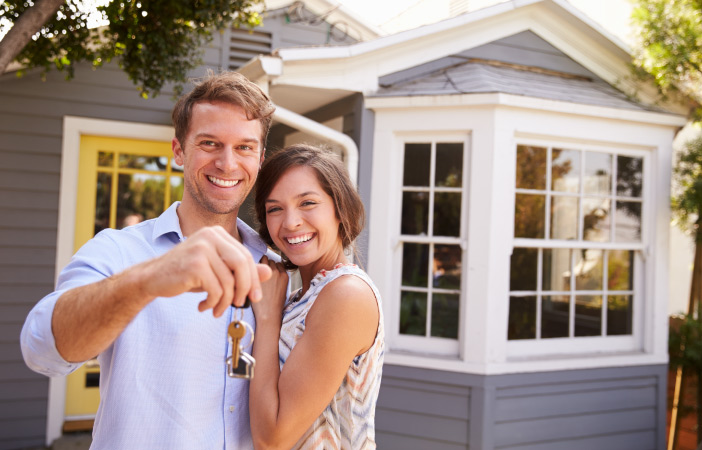 A happy couple shows off their house keys in front of their newly purchased home.
