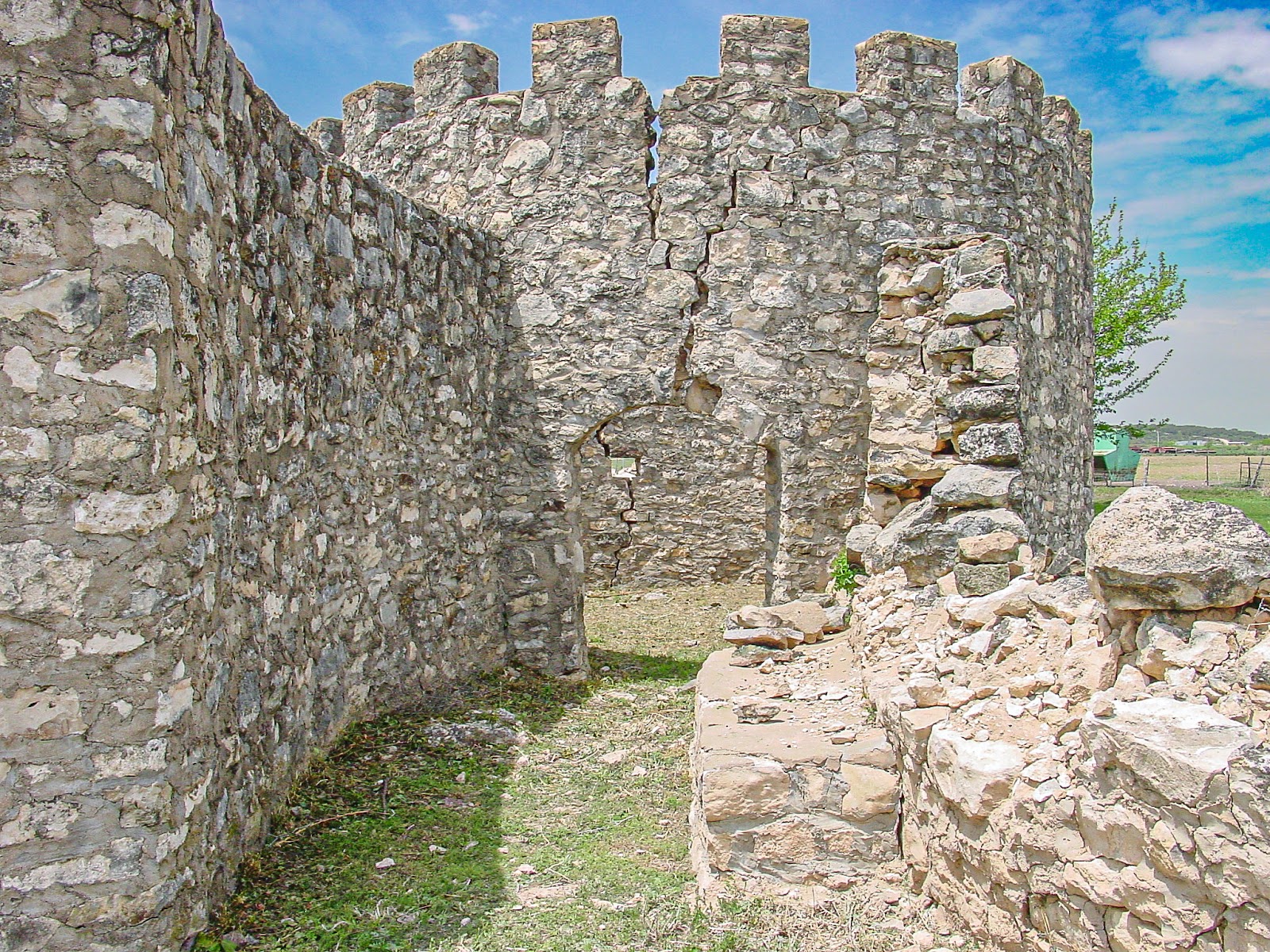 The ruins of an old fieldstone structure with an cylindrical turret, large crack in the wall and many scattered rocks.