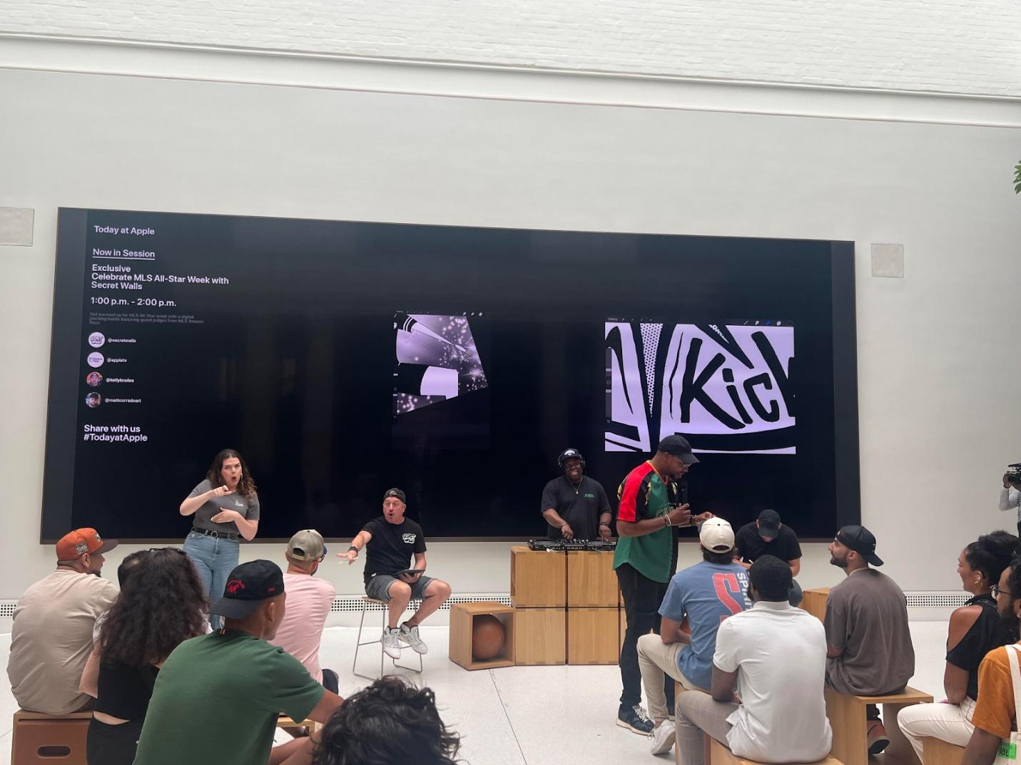 A group of people in a room with a large screen

Description automatically generated