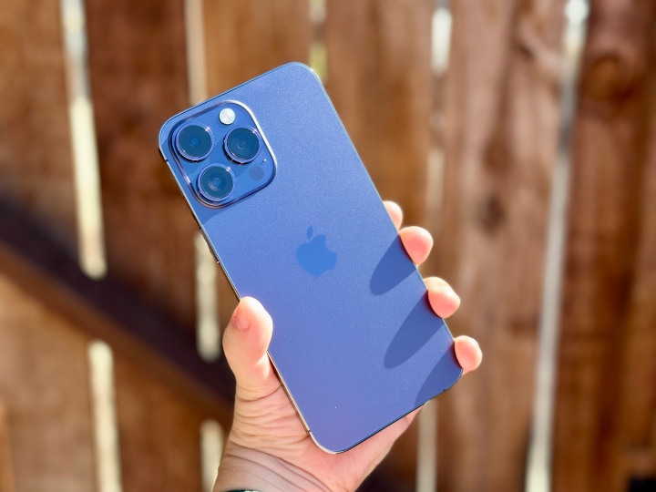 Deep Purple iPhone 14 Pro в руке на фоне деревянных ворот