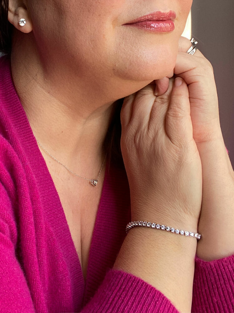 A closeup of Alison holding her hands near her face, showcasing James Allen diamond studs, tennis bracelet, and diamond pendant necklace.