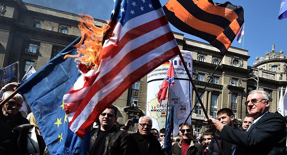 Serbian nationalist politician Vojislav Seselj (R) surrounded by his supporters holds a burning NATO flag during an anti-government rally on March 24, 2015, in front of the building of the former federal Interior Ministry in Belgrade