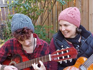 two people with ukeleles wearing cable knit hats