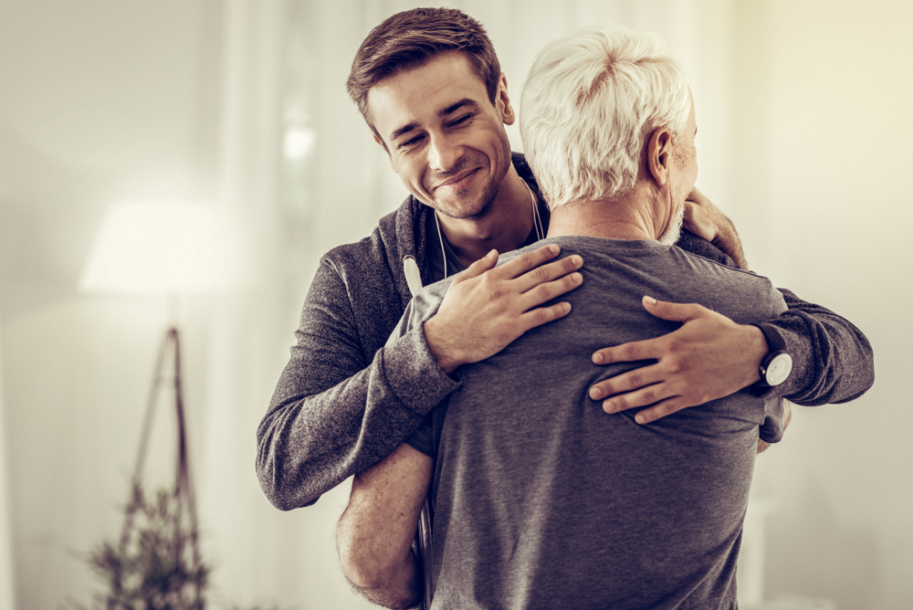 Smiling young man in hoodie embraces senior father.