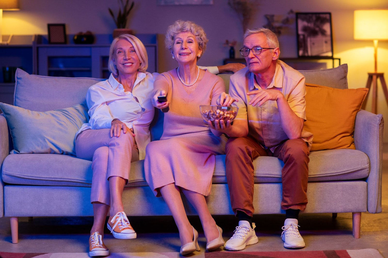 Three elderly people sitting on a couch and watching TV