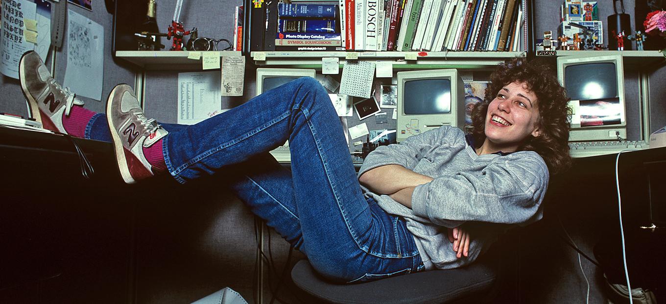 Photo of Susan Kare, one of the women in design featured in our article, legs up at her cubicle at Apple