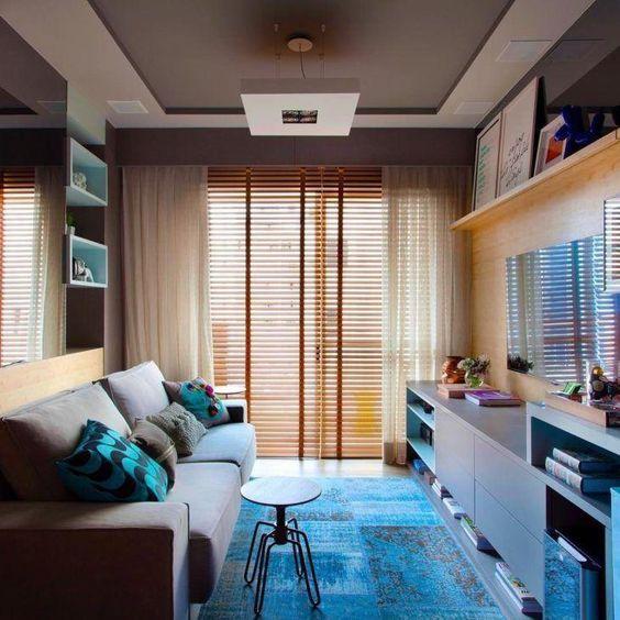 Sala com sofá cinza com almofadas coloridas,  nichos com enfeites, painel de TV com rack de madeira cinza com prateleiras com quadros pendentes e livros.