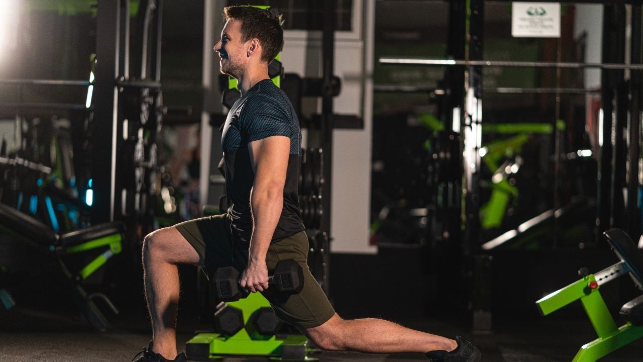 A man performs walking lunges with a pair of dumbbells.