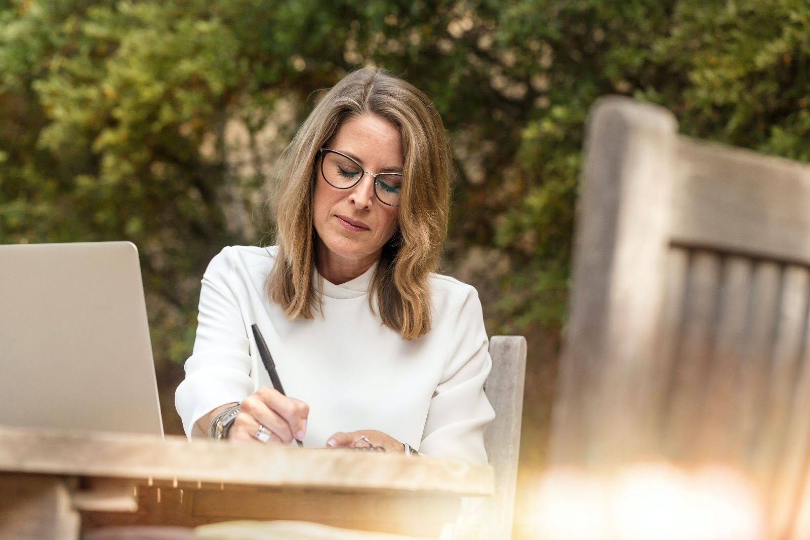 Older women sitting outside with her computer while she writes her transfer-on-death designation with a pen.