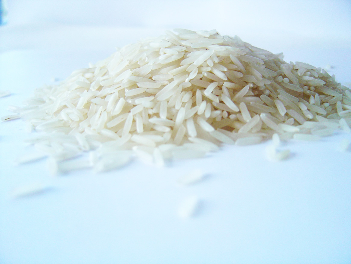 Grains of white rice lay in a pile on a white surface.