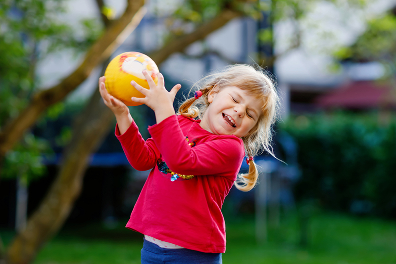 Little adorable toddler girl playing with ball outdoors