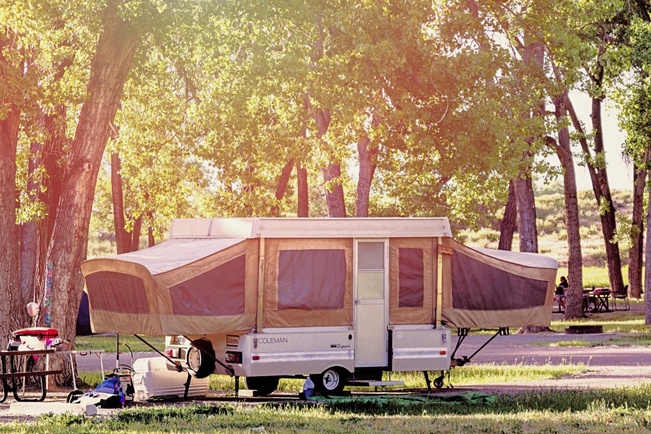 A pop-up travel trailer parked at a grassy campsite with its slide-outs extended