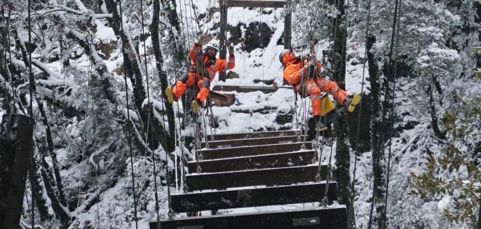 Abseil Access crew members brave winter snow to work on a suspension bridge on the Paparoa Track....