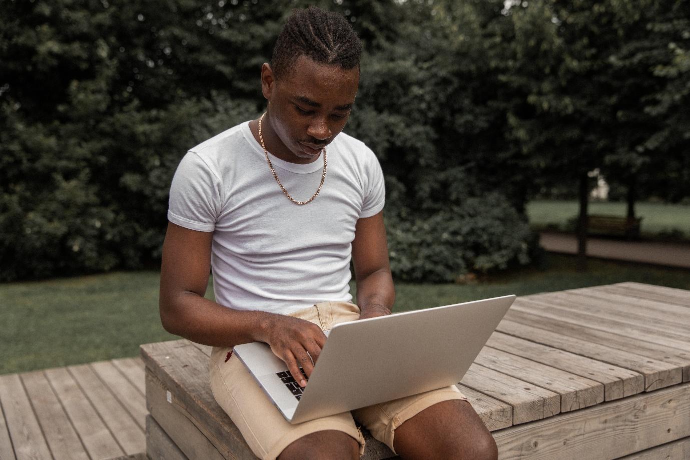 A person sitting on a bench using a computer

Description automatically generated