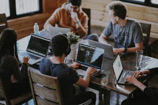 A group of people sitting around a table with laptops

Description automatically generated with medium confidence