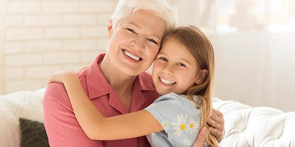 Happy granny with granddaughter hugging on sofa at home