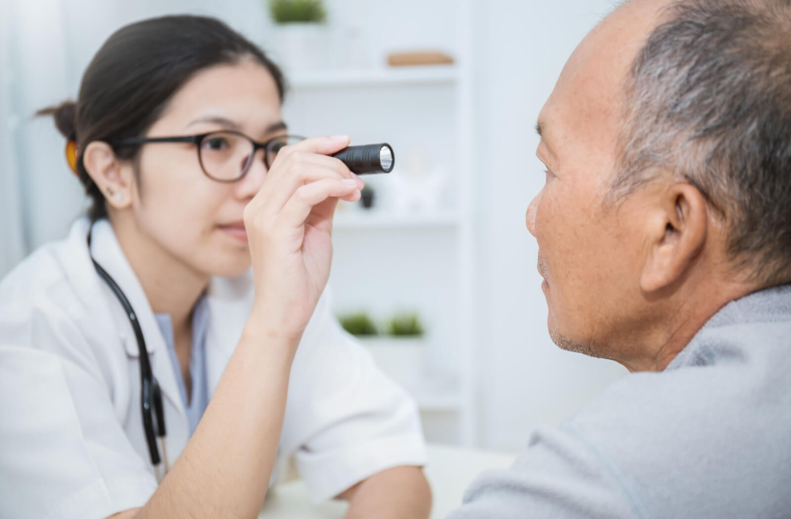 Optometrist looking at a male patient's eye with a light.