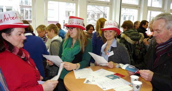 Streikende mit beschrifteten Hüten: »Gleiche Arbeit – gleicher Lohn« und »Gerechte Bezahlung«.