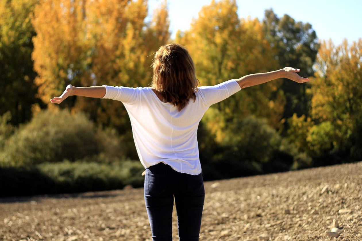 woman with arms outstretched in a field with trees in the distance