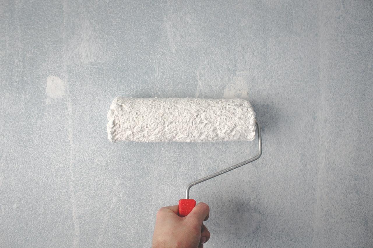 A person holding a paint roller against the white wall