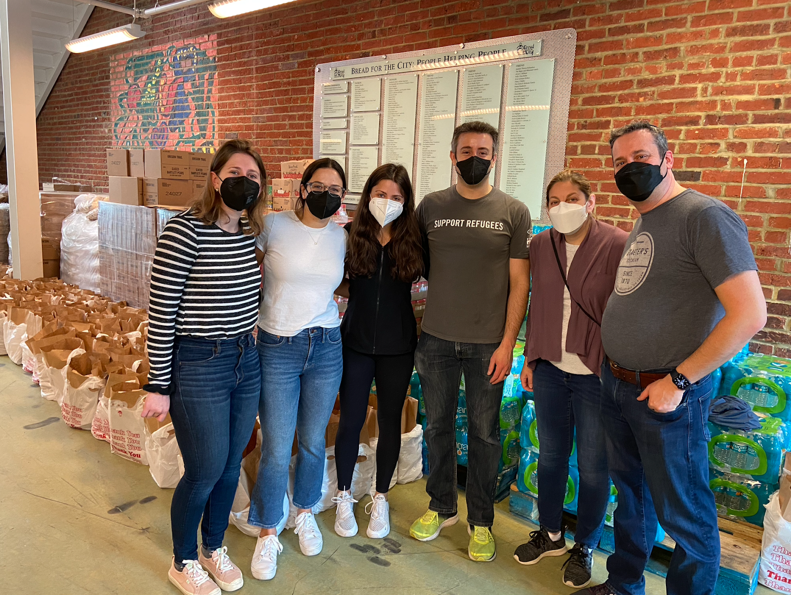 A group of people wearing masks pose in front of an array of bagged meals