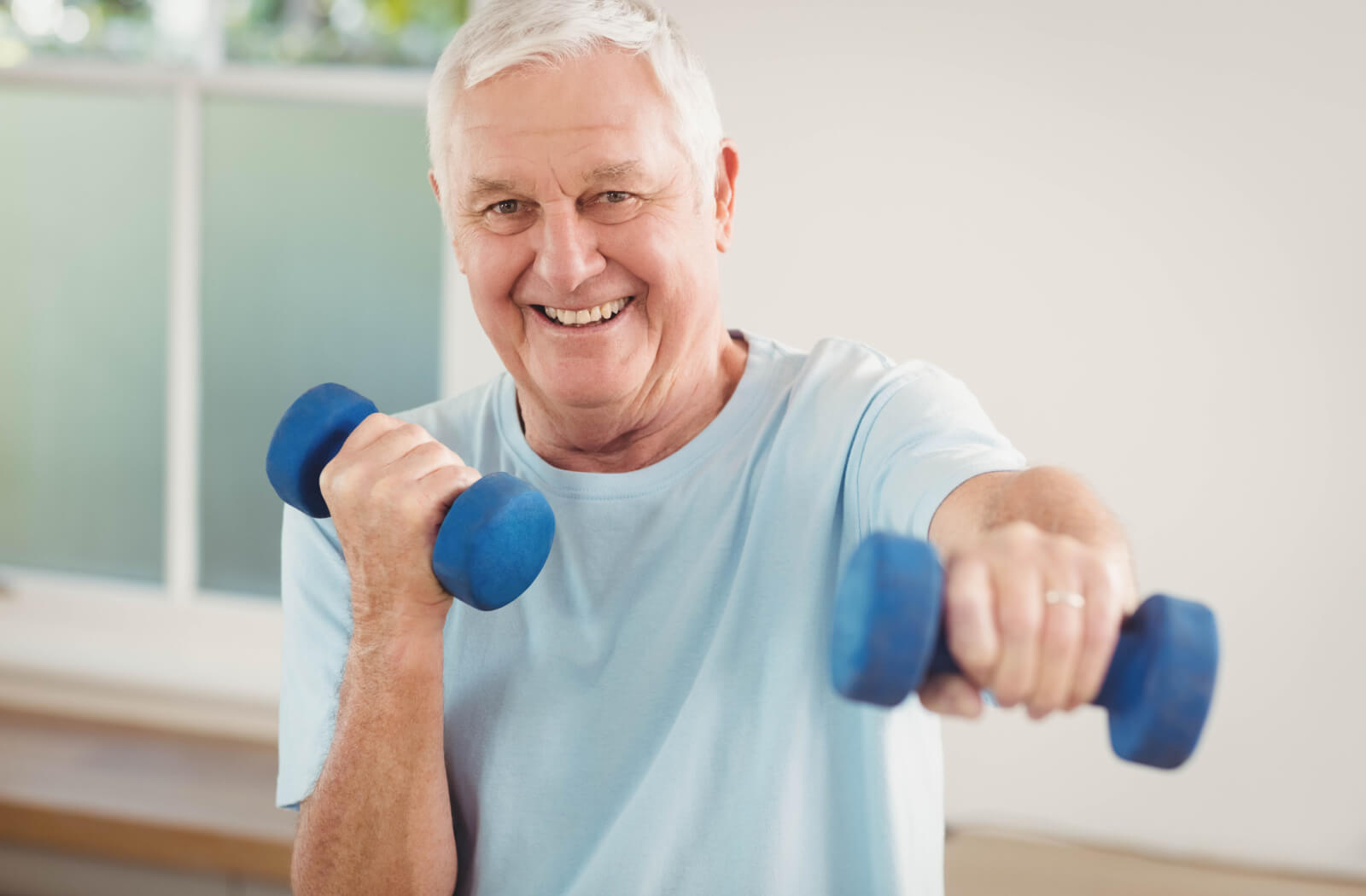 A senior man smiling with white hair wearing fitness clothes and exercising with dumbbells.