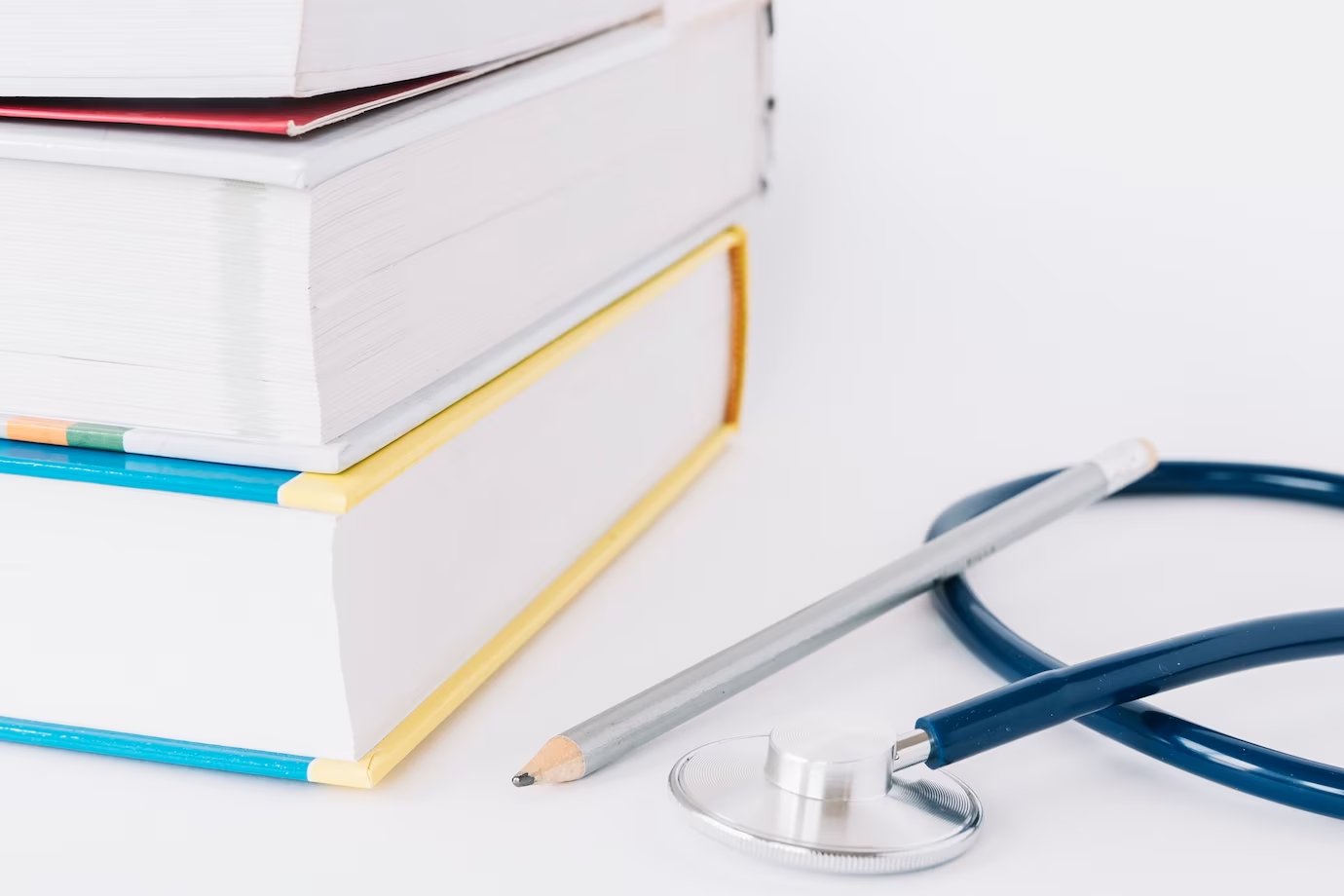 A stethoscope, pencil, and stack of books on a white surface - the essentials for applying to UK medical school from the UAE.