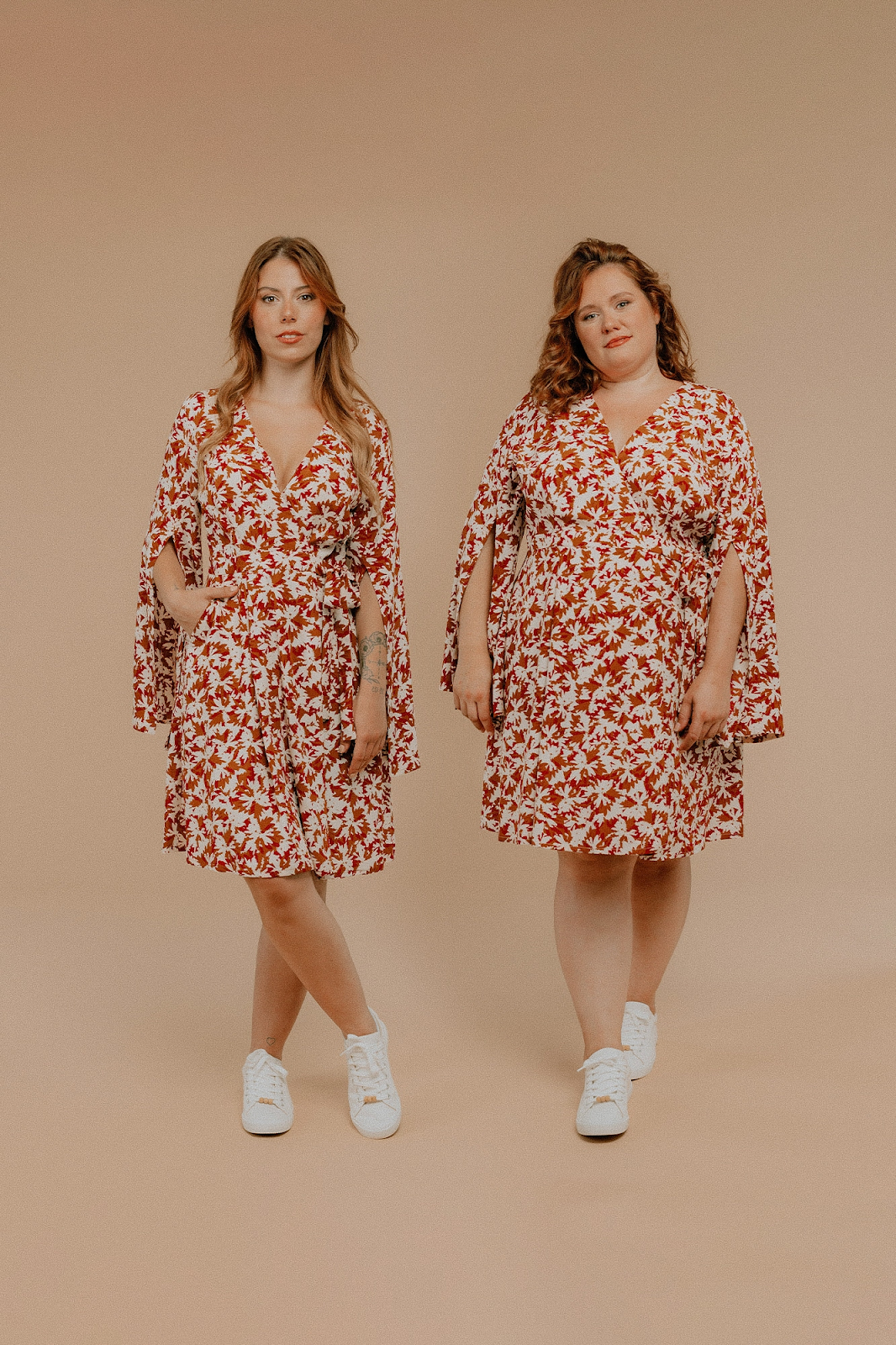 Two models wearing the same dress in the same fabric.  On the left a white person with long red hair wears a red/white patterned dress with long sleeves with front slits.  They are a medium build.  On the right, the same dress is worn by a model with a plus size build.
