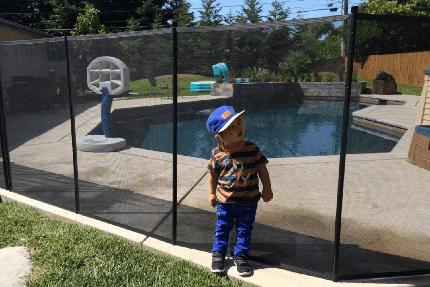 Young boy leaning against a removable mesh pool fence