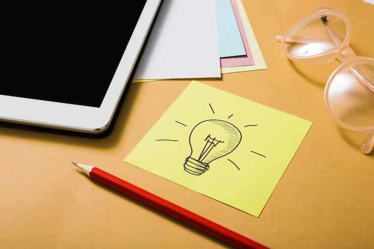 A hand-drawn lightbulb symbolizes an idea, with a pencil and digital tablet on an orange backdrop.