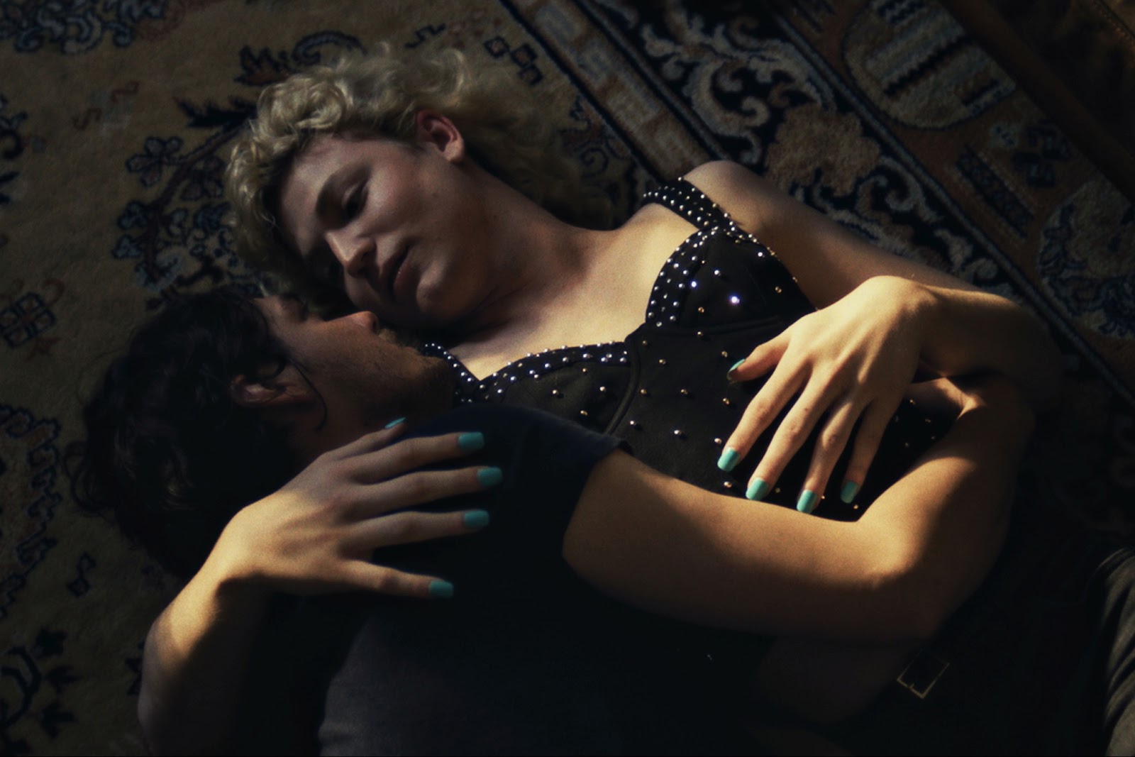 From the film Till the End of the Night, two people lay on a ornate rug on the floor, holding on another closely and looking into each other's eyes.
