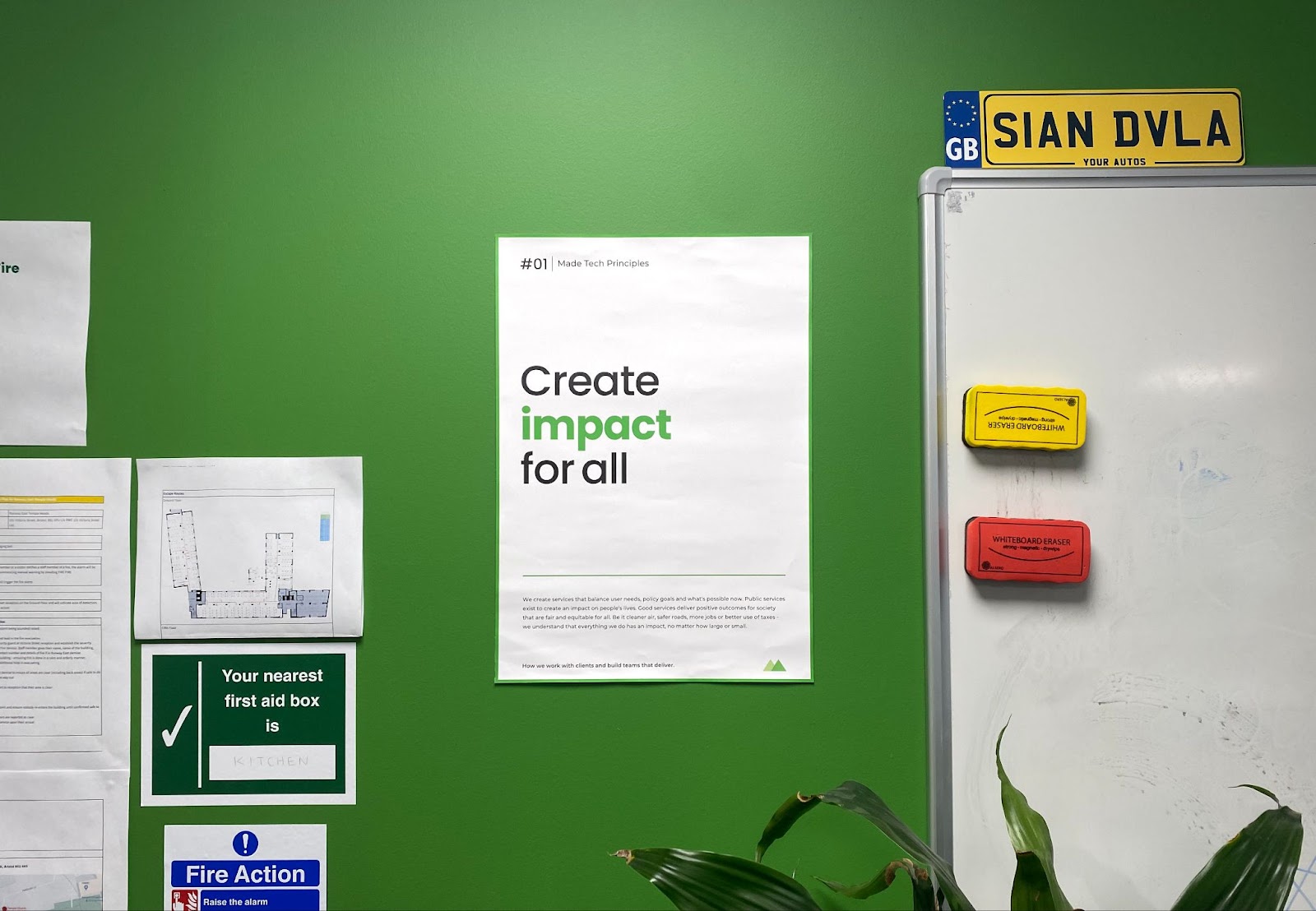 In an office room with a green wall is a poster of the 'create impact for all' principle.