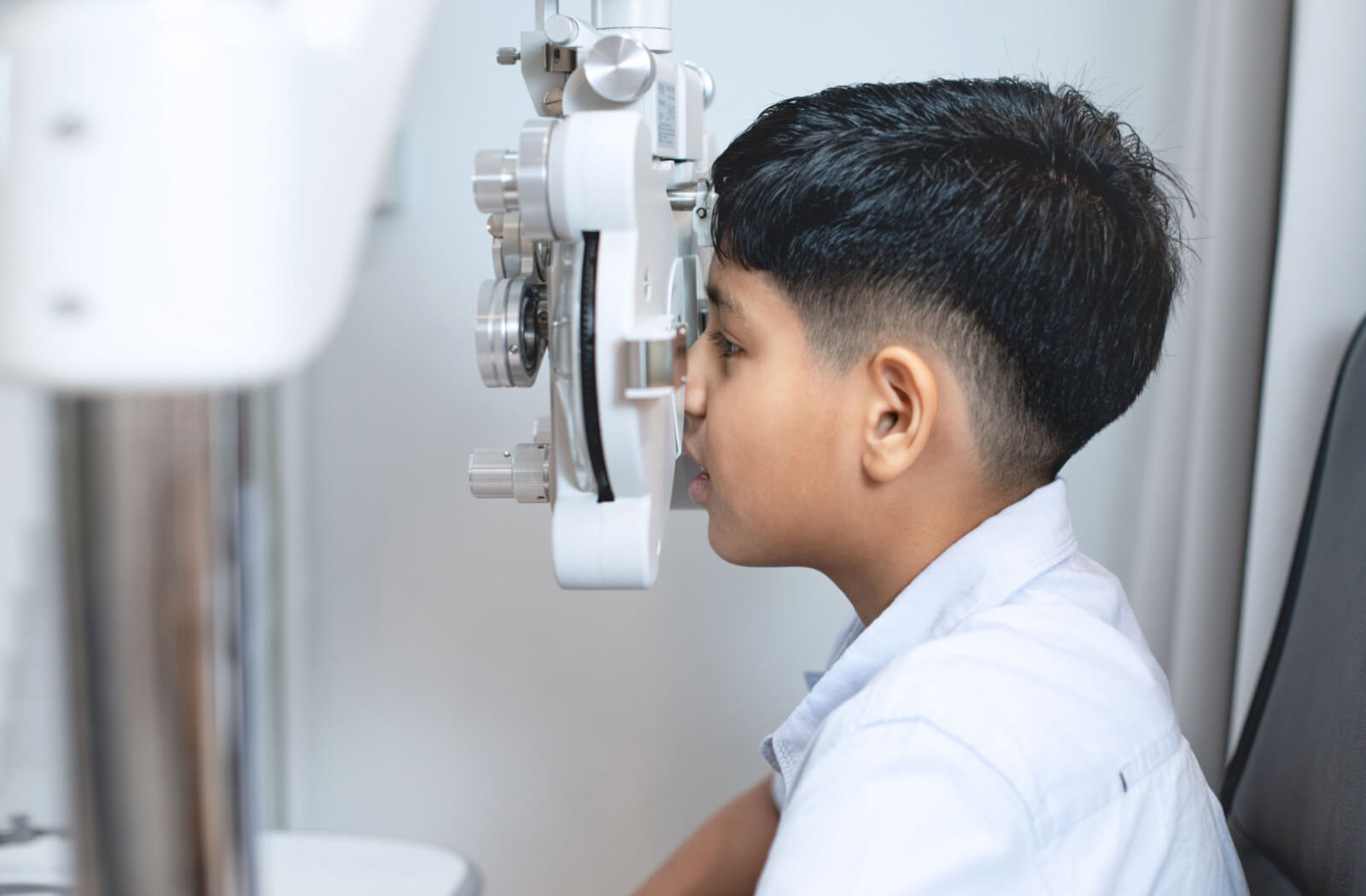 A child sitting in an ophthalmologist's office looking into a machine that tests his vision