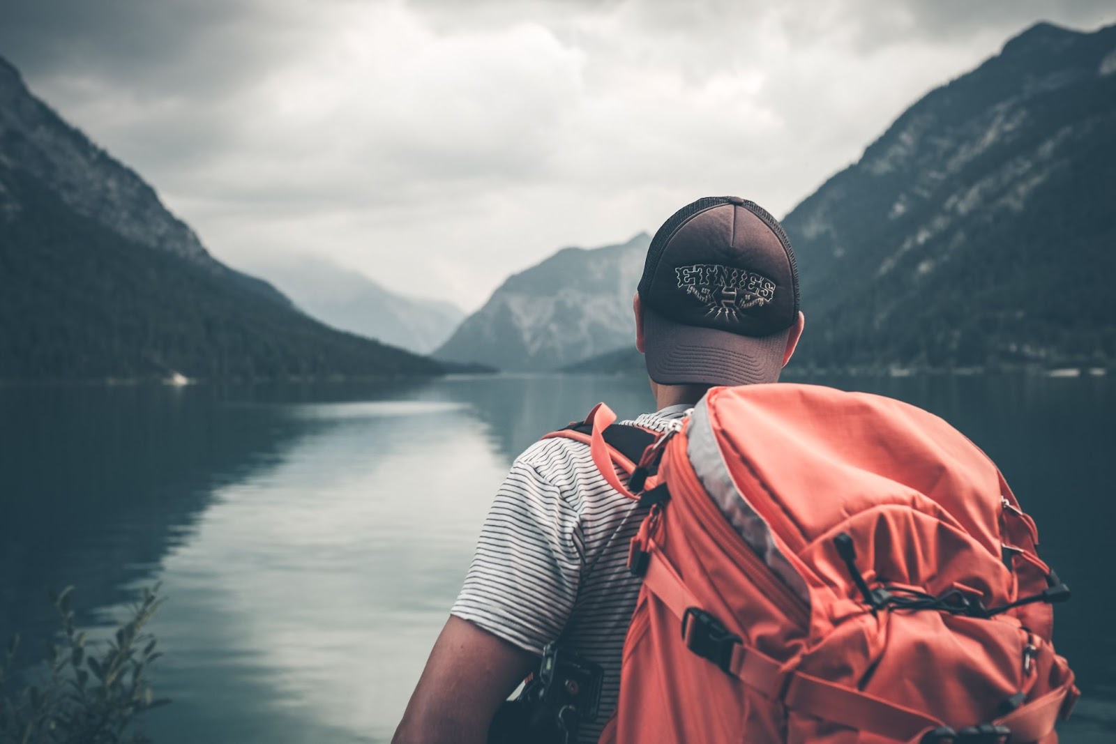 Man looking at a lake wearing an orange backpack 