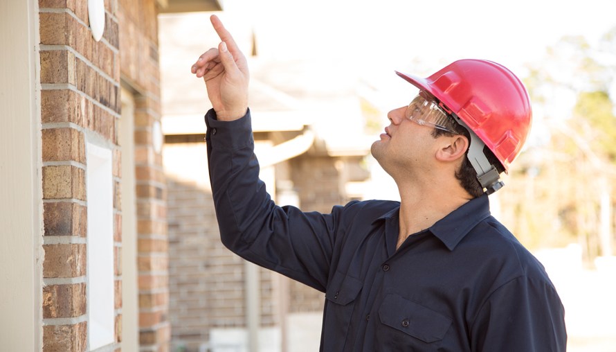 Man wearing hard hat and pointing to something on exterior of home