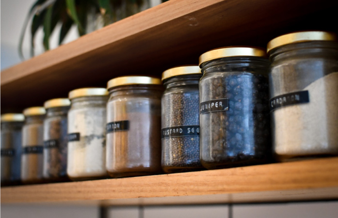 An organized pantry shelf with goods stored in reusable glass containers and clearly labeled.