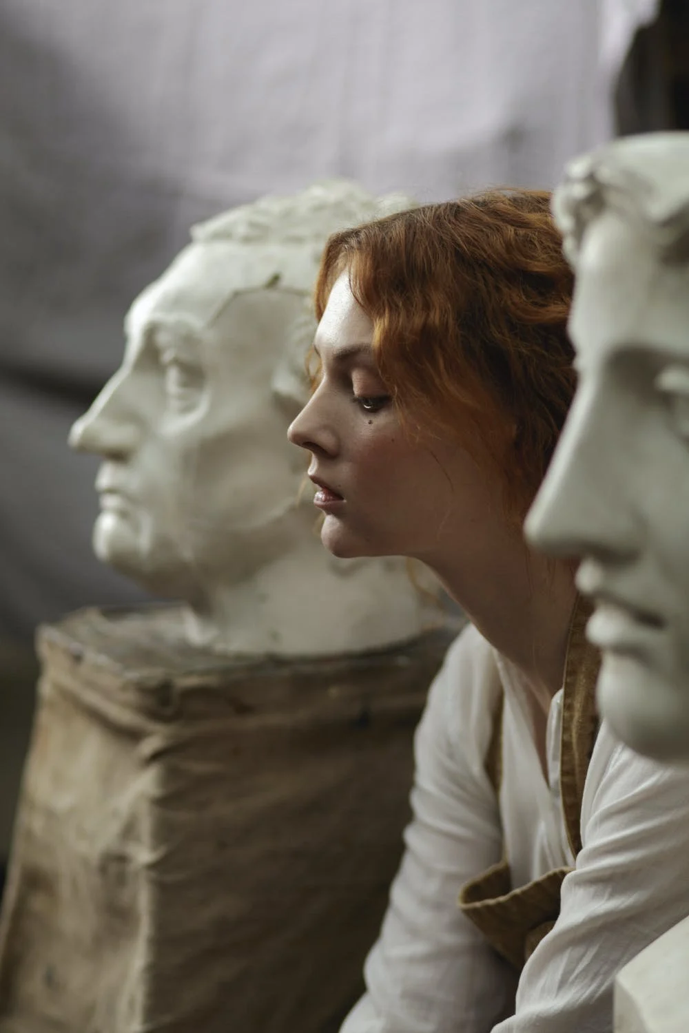 image of a woman sat in between two statue busts of a grecian style