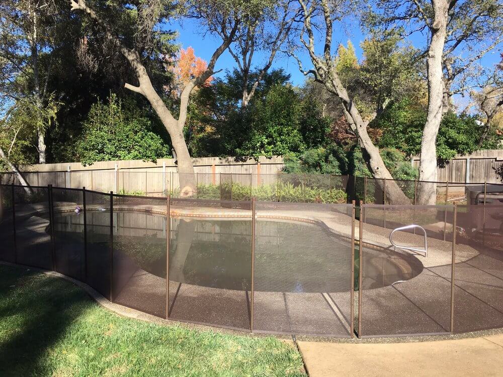 Brown mesh pool fence surrounding a backyard swimming pool