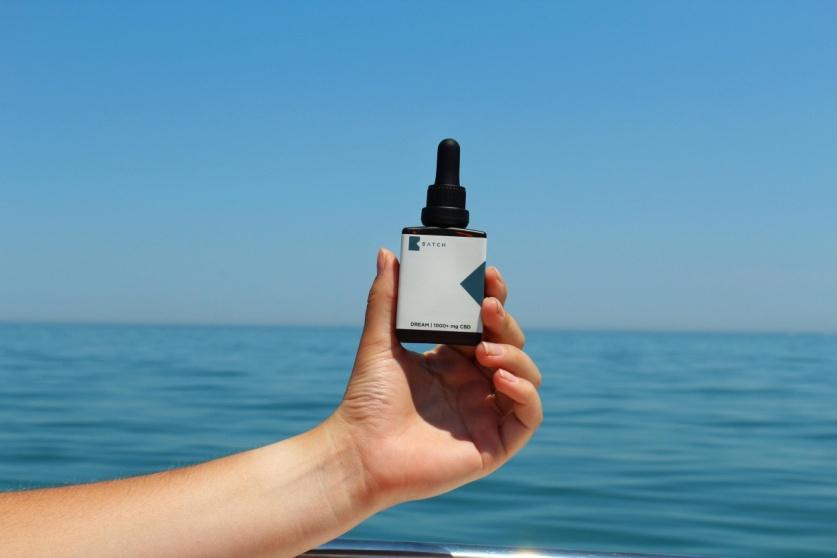 hand holding a CBD skin care product with the ocean in the background