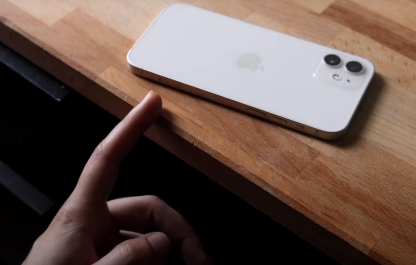 a finger pointing at an iPhone on a wooden table