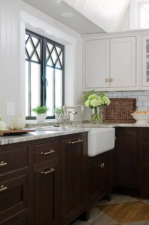 farmhouse kitchen with two toned cabinets in dark brown and white. the cabinets are shaker style with simple silver hardware. a farmhouse sink overlooks the window, giving it a country rustic feel