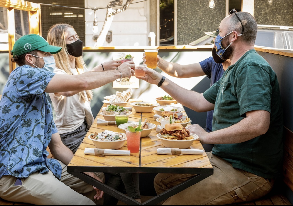 People wearing masks and cheers-ing drinks with food on a patio