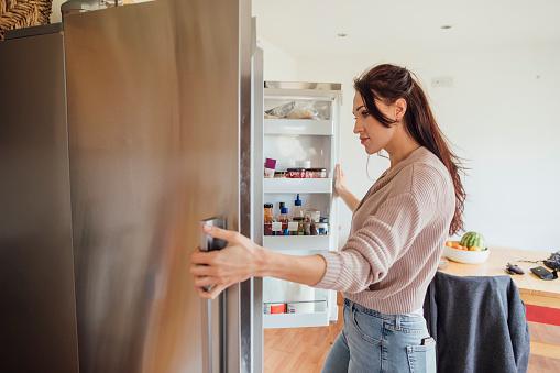 WeServe, woman staring into a silver fridge standing in the kitchen inspecting to see if it needs a repair or a new appliance installation