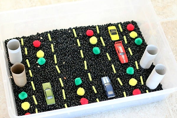 car sensory bin with black beans and toy cars