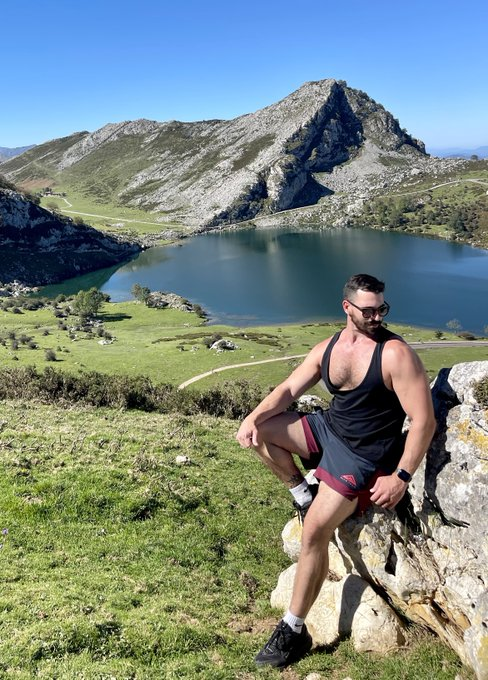 Thick Macho posing outside with a hill and body of water in the background while wearing athletic gym wear