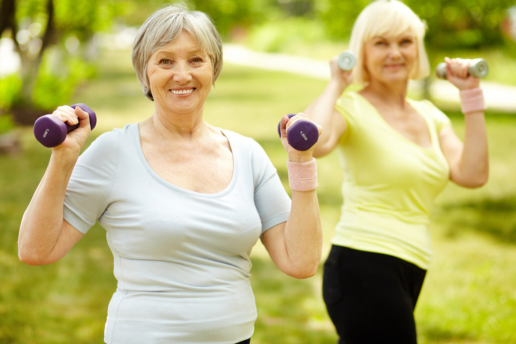 Two older women lifting weights at a park.