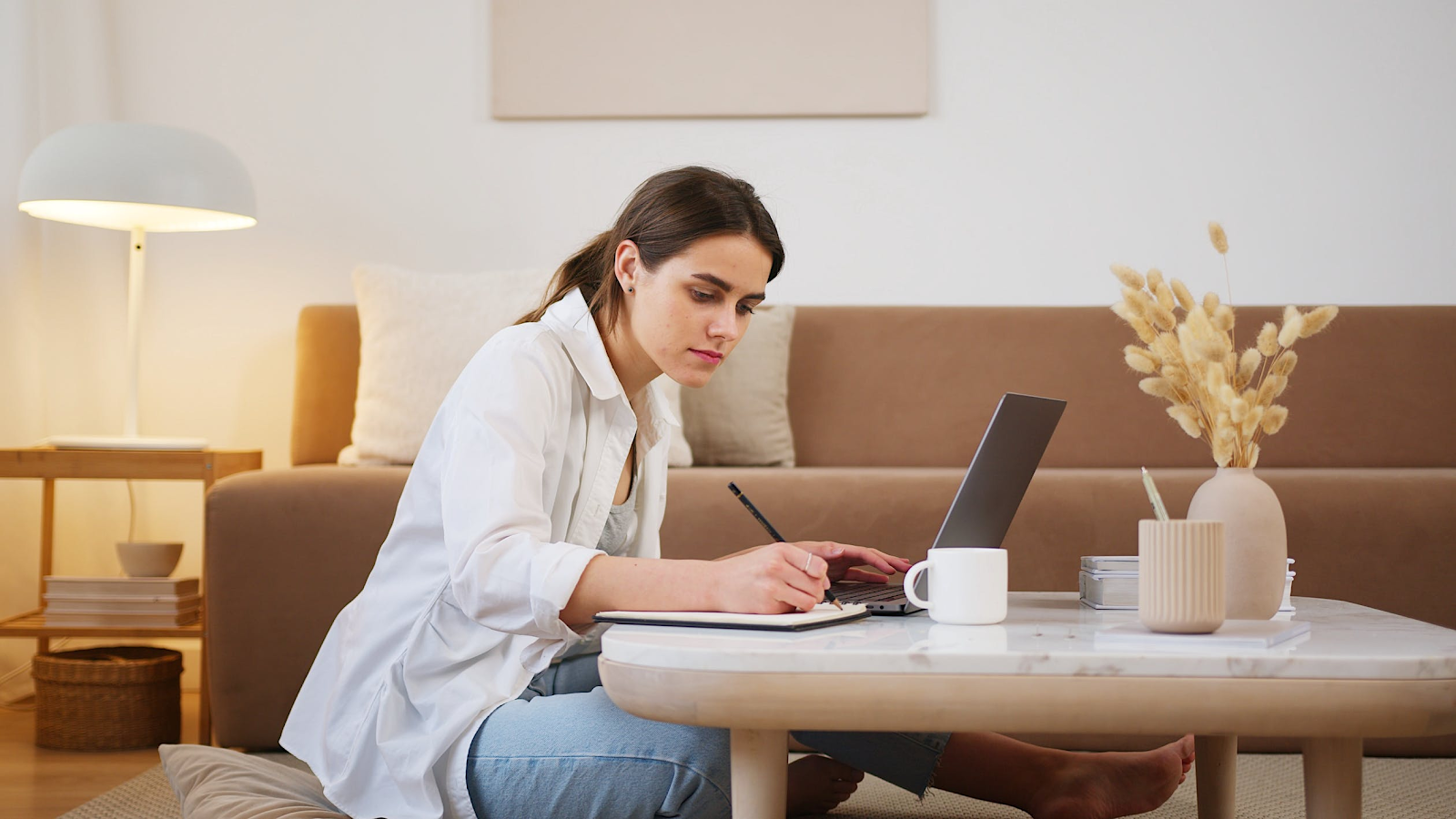 Woman in white writing down notes at her living room coffee table