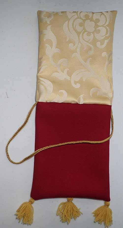 Both layers of the bag are visible sewn together, with the cream silk layer at the top of the image and the red wool layer with its cord and tassels at the bottom. The corners of both layers have been pushed out with a thin tool to appear very squared off.