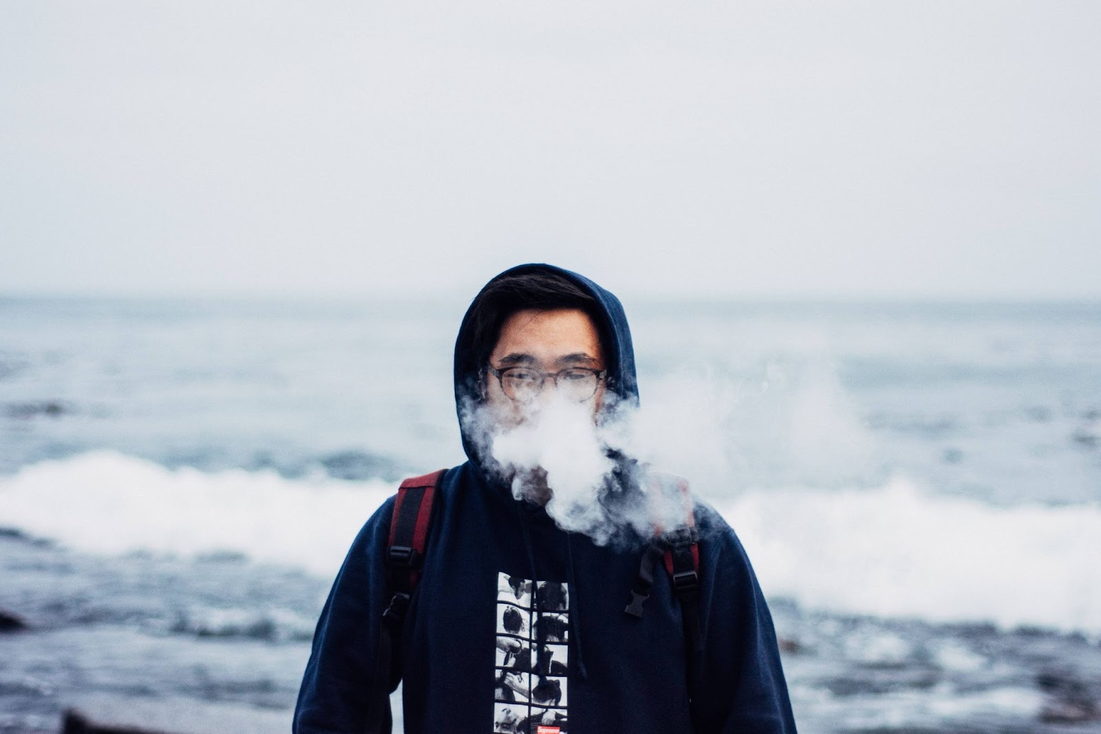 A man in hoodie vaping at the beach
